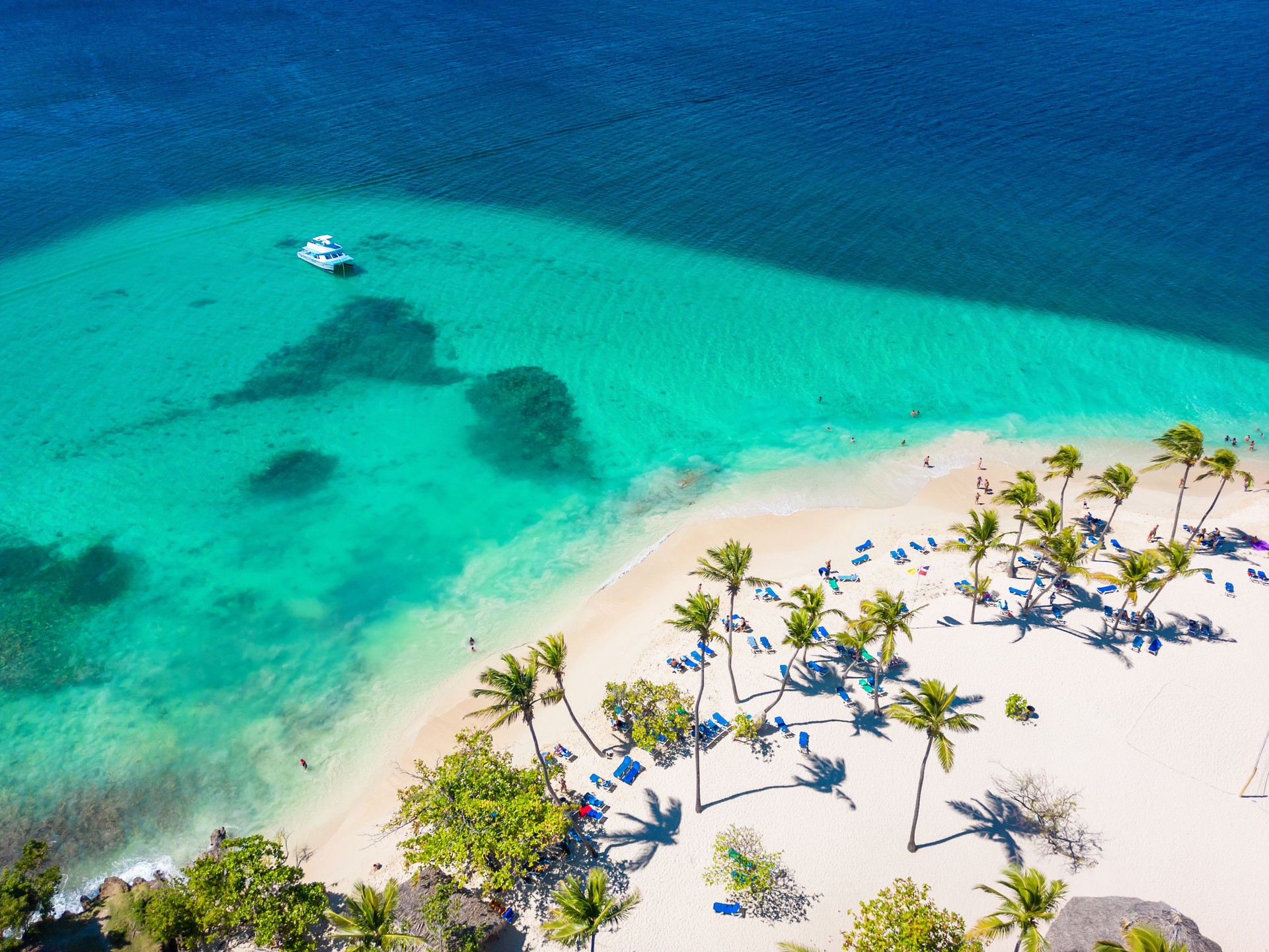 Aerial view of tropical beach with turquoise color of the water, chairs and palm trees. Yacht anchored near the shore. Best summer vacations on the Caribbean